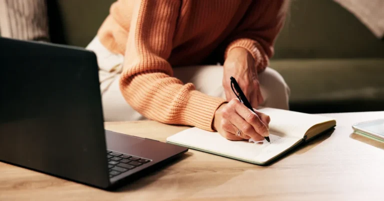 Woman writing in a notebook next to an open computer